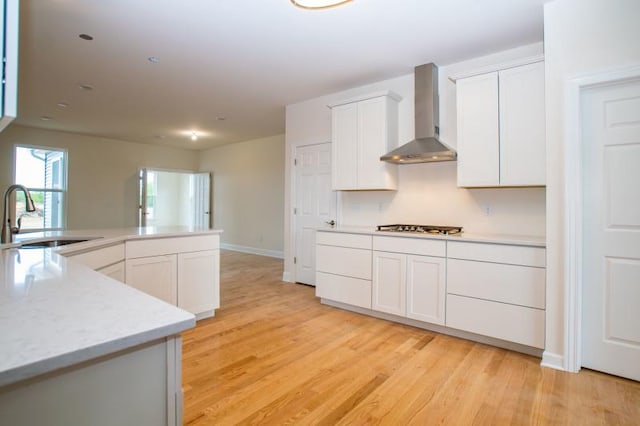 kitchen featuring light hardwood / wood-style floors, stainless steel gas cooktop, wall chimney range hood, white cabinets, and sink