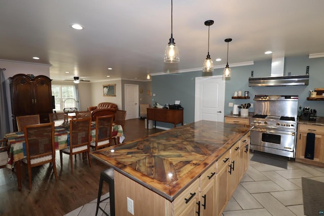 kitchen featuring crown molding, a center island, high end stove, ceiling fan, and wall chimney range hood