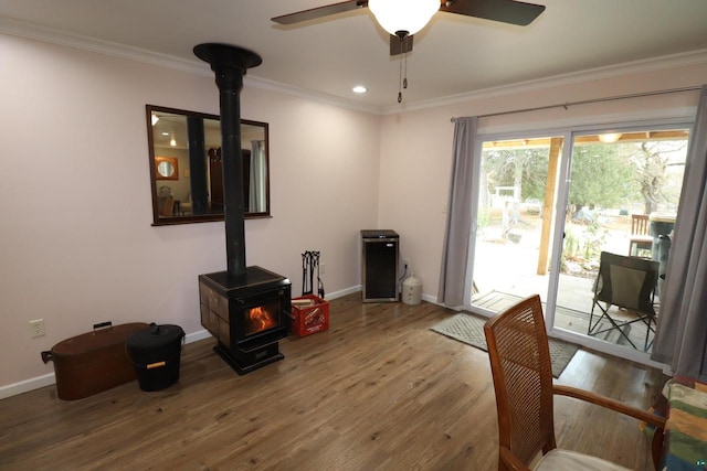 interior space featuring ceiling fan, a wood stove, ornamental molding, and hardwood / wood-style flooring