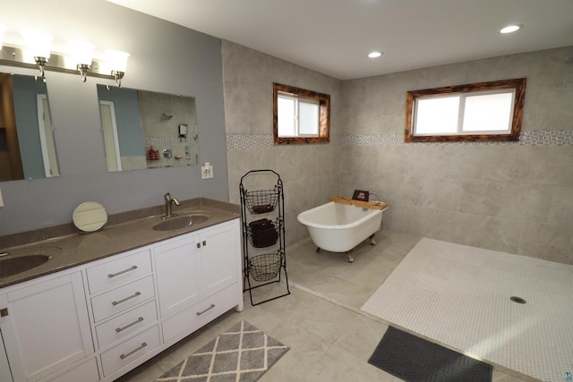 bathroom with tile walls, tile floors, dual sinks, large vanity, and a bathtub