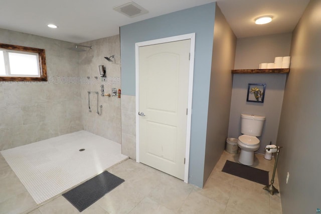 bathroom featuring toilet, a tile shower, and tile flooring