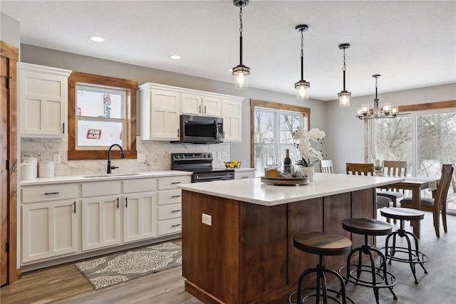 kitchen with sink, decorative light fixtures, electric range, a kitchen island, and white cabinets