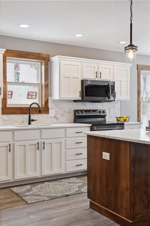 kitchen featuring range with electric stovetop, white cabinetry, hanging light fixtures, and sink