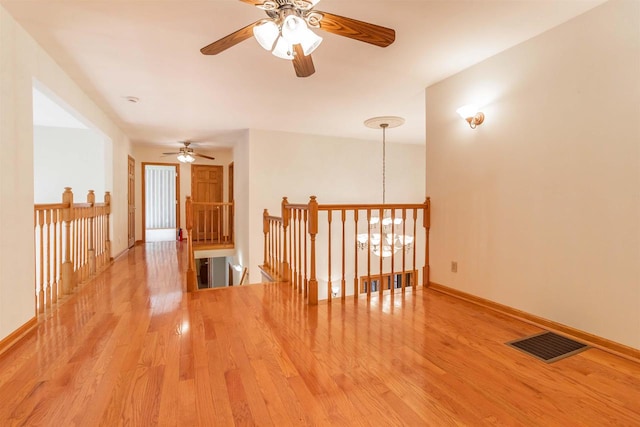 spare room with ceiling fan with notable chandelier and light wood-type flooring