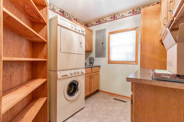 clothes washing area featuring stacked washing maching and dryer, light tile floors, and cabinets