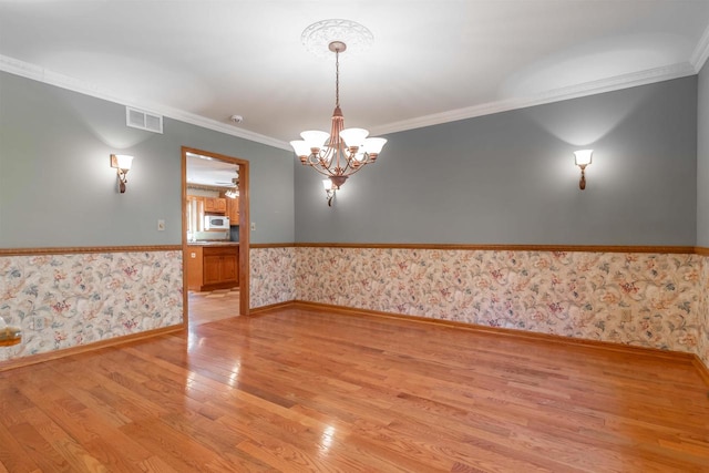 unfurnished room featuring crown molding, light wood-type flooring, and an inviting chandelier