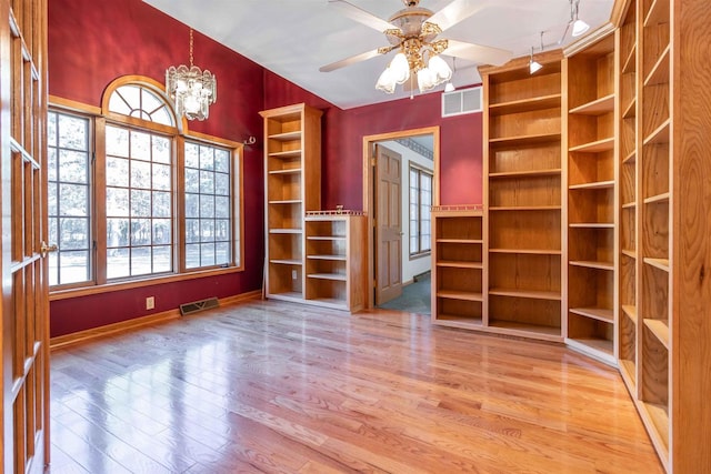 empty room featuring ceiling fan with notable chandelier, a healthy amount of sunlight, and light wood-type flooring