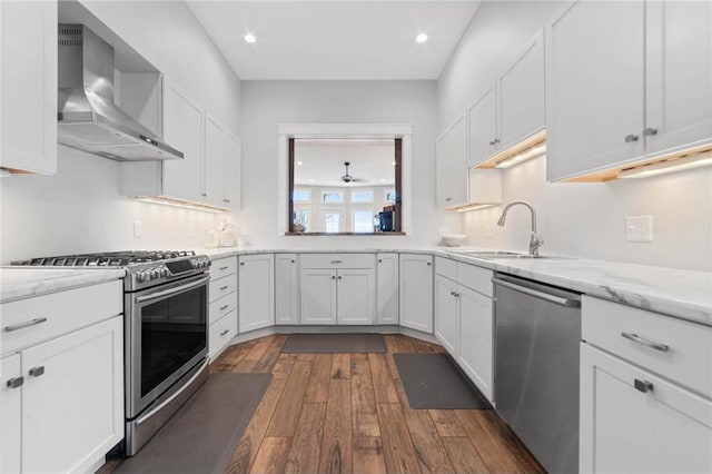 kitchen featuring dark wood-type flooring, appliances with stainless steel finishes, white cabinetry, wall chimney exhaust hood, and sink