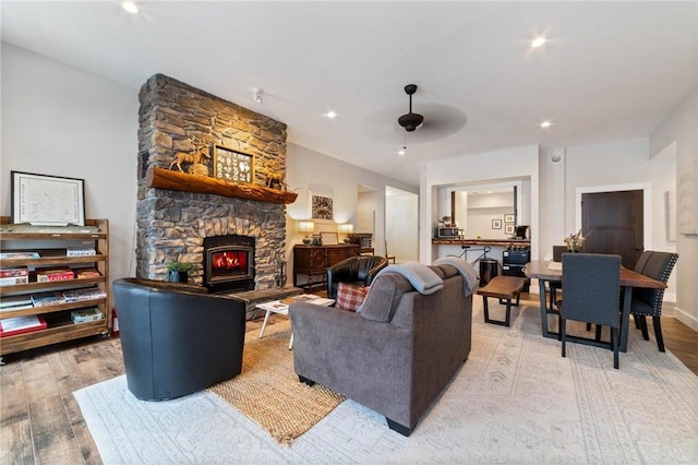 living room featuring ceiling fan, light hardwood / wood-style flooring, and a stone fireplace