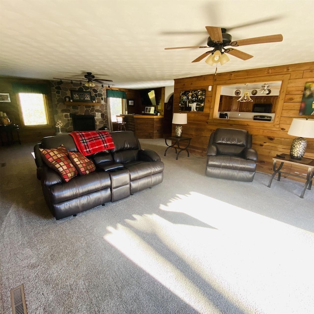 carpeted living room featuring ceiling fan, wooden walls, and a fireplace