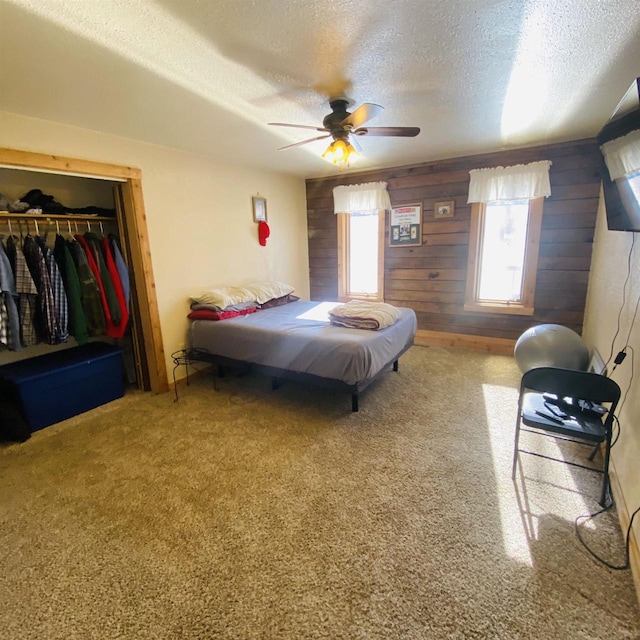 carpeted bedroom with wood walls, a closet, ceiling fan, and a textured ceiling