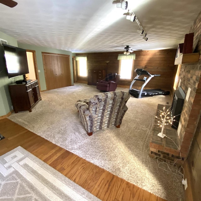 carpeted living room featuring ceiling fan, a brick fireplace, rail lighting, and wood walls