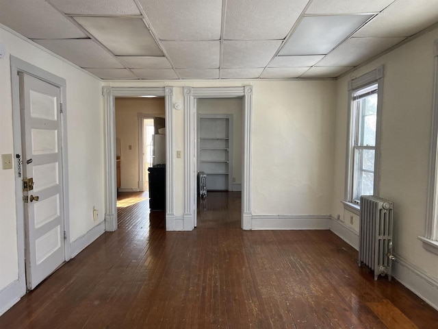 unfurnished room with dark hardwood / wood-style floors, radiator, and a drop ceiling