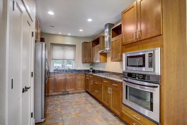 kitchen with dark tile floors, sink, stainless steel appliances, dark stone counters, and wall chimney exhaust hood