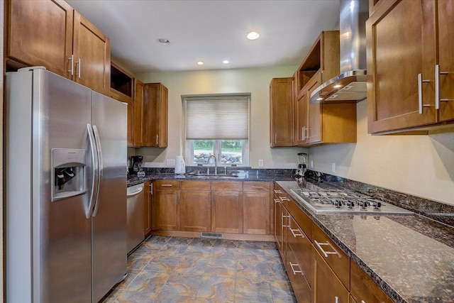 kitchen with dark stone counters, appliances with stainless steel finishes, dark tile flooring, wall chimney range hood, and sink