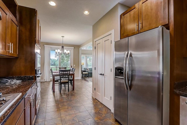 kitchen featuring appliances with stainless steel finishes, hanging light fixtures, a notable chandelier, dark stone countertops, and dark tile flooring