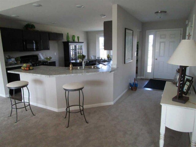 kitchen featuring a breakfast bar, carpet floors, kitchen peninsula, black appliances, and sink