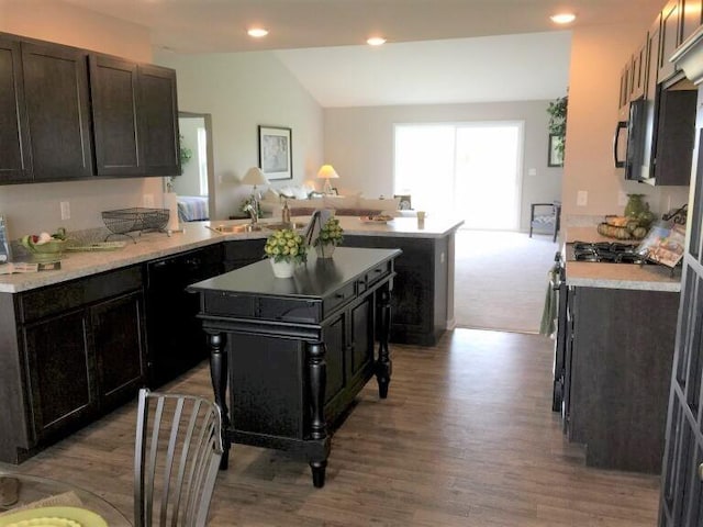 kitchen featuring kitchen peninsula, a kitchen island, vaulted ceiling, and black dishwasher