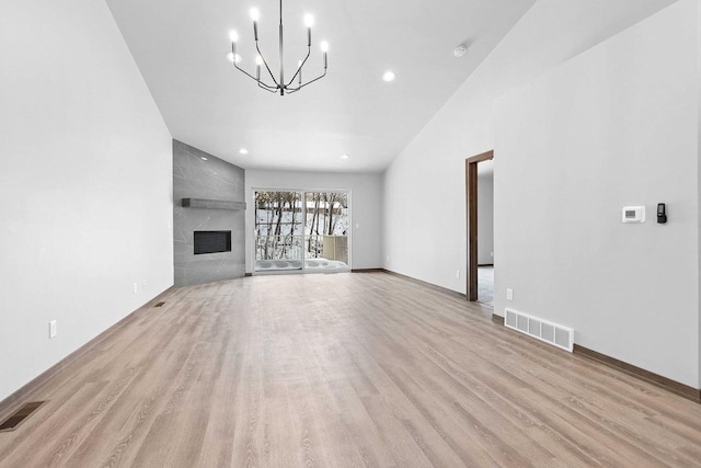 unfurnished living room with a notable chandelier, lofted ceiling, a large fireplace, and light wood-type flooring