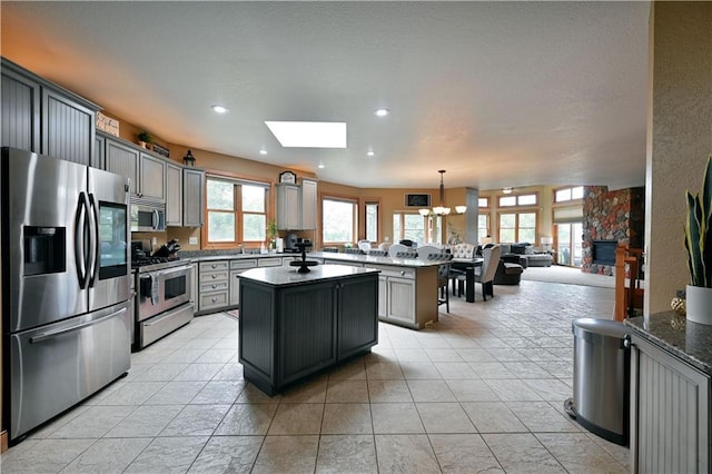 kitchen featuring an inviting chandelier, a skylight, a kitchen island, stainless steel appliances, and gray cabinetry