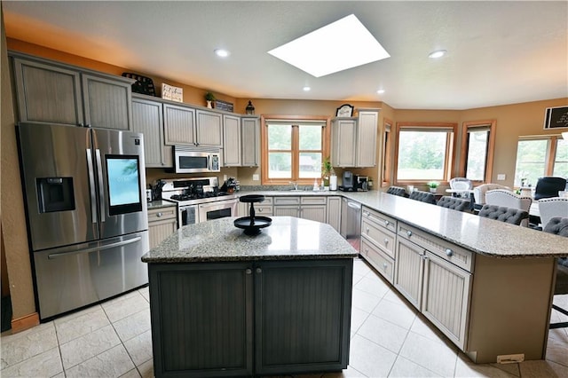 kitchen featuring a skylight, stainless steel appliances, a center island, and light tile floors