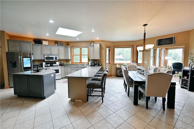 kitchen featuring appliances with stainless steel finishes, hanging light fixtures, an inviting chandelier, a skylight, and gray cabinets