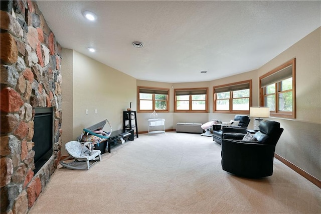 living room with a textured ceiling, light colored carpet, and a stone fireplace