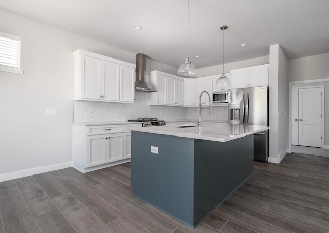 kitchen featuring white cabinets, appliances with stainless steel finishes, a kitchen island with sink, and wall chimney range hood