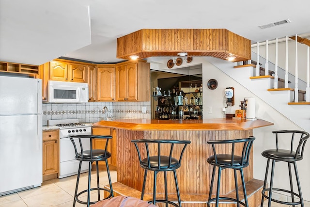W1188 Spring Grove Rd, Green Lake, WI 54971 - kitchen with kitchen peninsula, white appliances, light tile floors, backsplash, and a breakfast bar area
