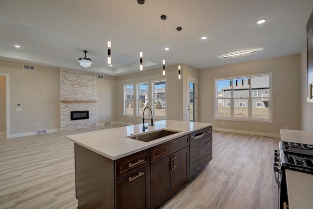 kitchen featuring light hardwood / wood-style floors, decorative light fixtures, sink, a stone fireplace, and a kitchen island with sink