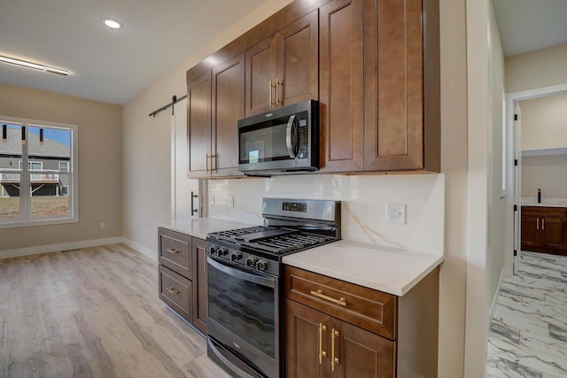 kitchen featuring backsplash, a barn door, stainless steel appliances, and light hardwood / wood-style flooring