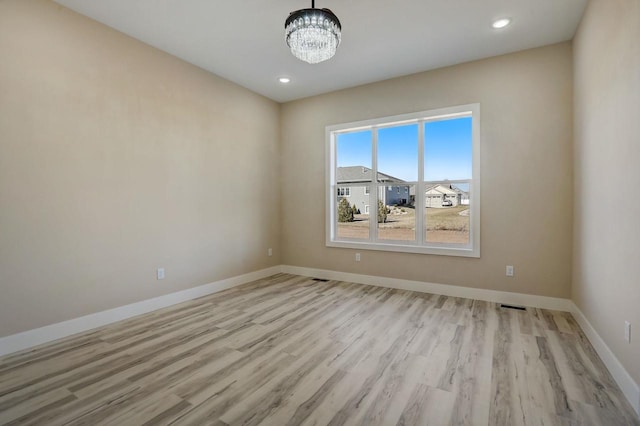 empty room with light hardwood / wood-style flooring and a notable chandelier