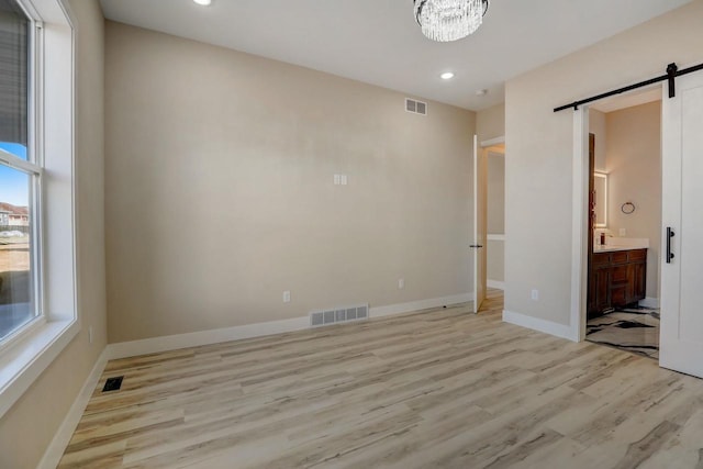 unfurnished bedroom featuring a barn door, light hardwood / wood-style floors, multiple windows, and ensuite bath