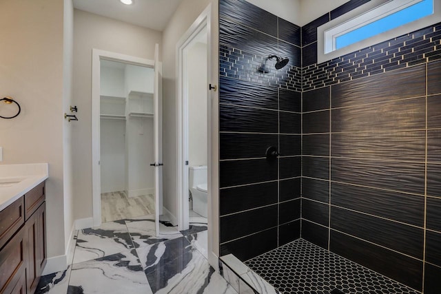 bathroom featuring toilet, tile flooring, a tile shower, and vanity