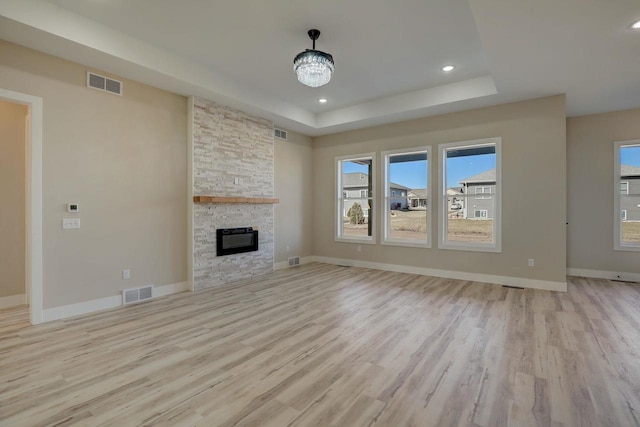 unfurnished living room with an inviting chandelier, light hardwood / wood-style floors, a tray ceiling, and a fireplace