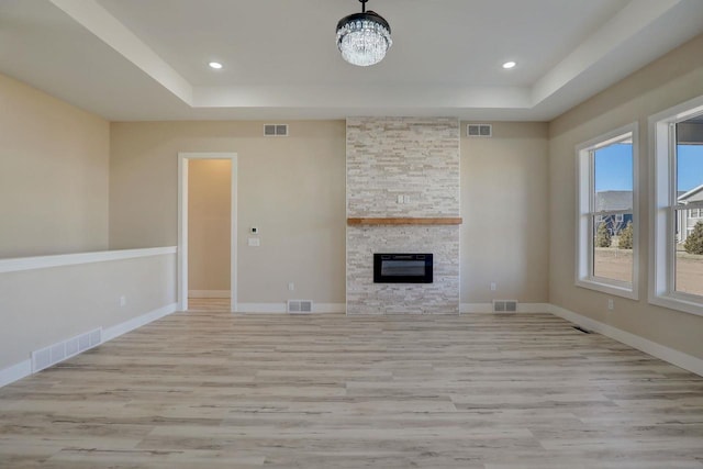 unfurnished living room featuring light hardwood / wood-style flooring, a raised ceiling, a notable chandelier, and a fireplace