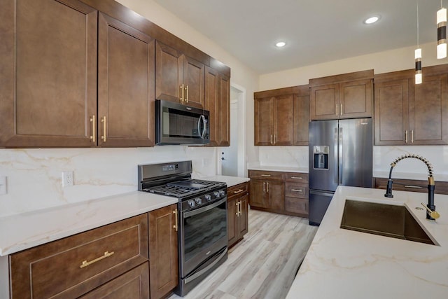 kitchen featuring appliances with stainless steel finishes, hanging light fixtures, light stone counters, light hardwood / wood-style floors, and sink