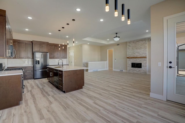 kitchen with hanging light fixtures, a fireplace, light wood-type flooring, stainless steel appliances, and a center island with sink