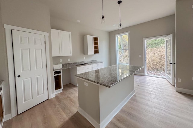 kitchen featuring stone countertops, light hardwood / wood-style flooring, a center island, white cabinets, and pendant lighting