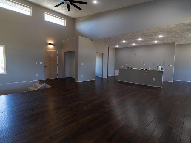 unfurnished living room with dark hardwood / wood-style flooring, ceiling fan, and a high ceiling