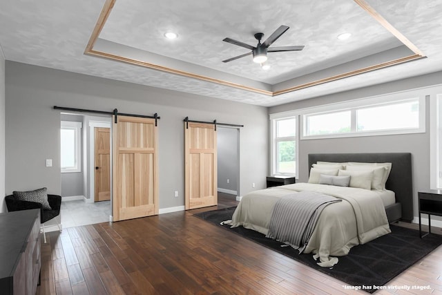 bedroom with a barn door, a raised ceiling, hardwood / wood-style floors, and a textured ceiling