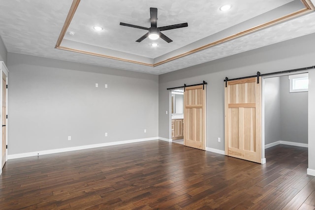 unfurnished bedroom with a raised ceiling, a barn door, dark wood-type flooring, and ceiling fan