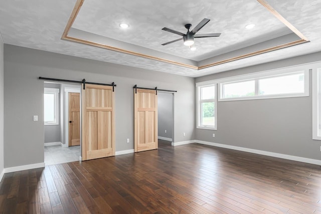 unfurnished bedroom with dark wood-type flooring, a barn door, and a raised ceiling