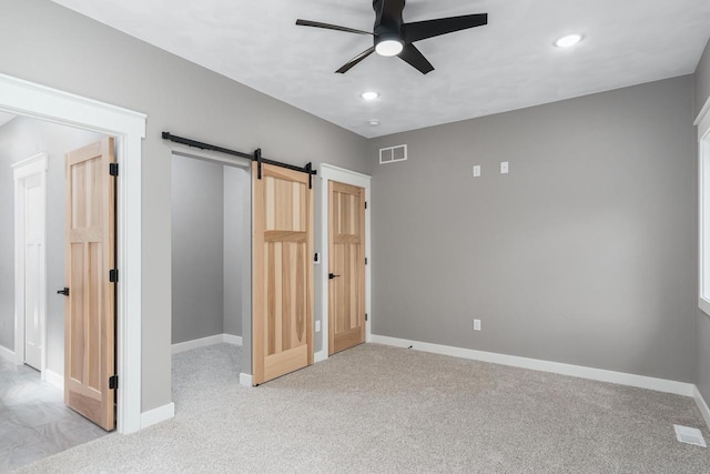 unfurnished bedroom with light carpet, a barn door, and ceiling fan