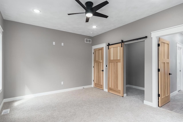 unfurnished bedroom with light carpet, a barn door, and ceiling fan