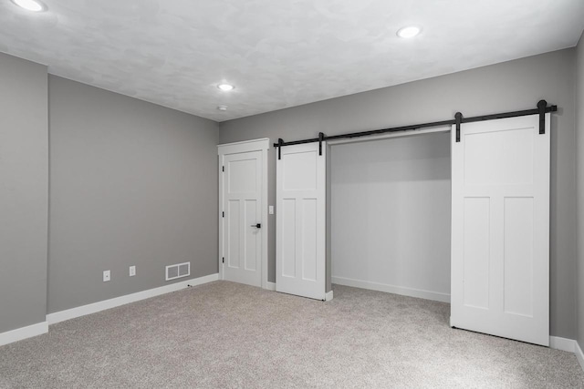 unfurnished bedroom with light carpet, a closet, and a barn door