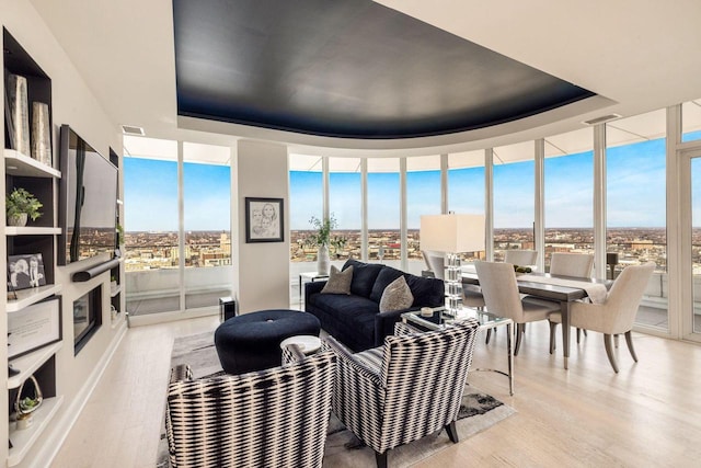 living room with a wall of windows, a tray ceiling, and light hardwood / wood-style floors