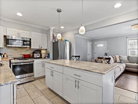 kitchen featuring appliances with stainless steel finishes, backsplash, white cabinetry, and decorative light fixtures