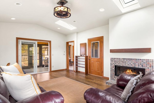 living room featuring a tiled fireplace, dark wood-type flooring, and vaulted ceiling with skylight