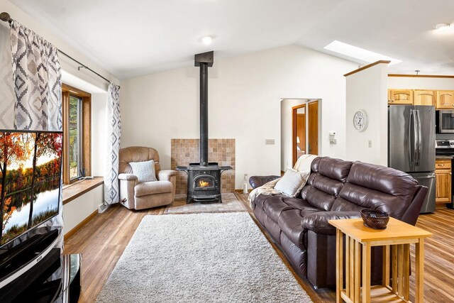 living room with a wood stove, vaulted ceiling with skylight, and light hardwood / wood-style flooring